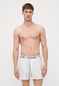 Boxers blancs avec des rayures grises verticales, dotés d'une ceinture élastique noire étiquetée "JACK & JONES." Fabriqués en tissu léger.