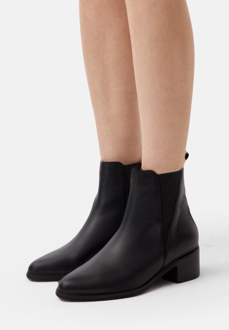 Mustad nahast ankle-kingad terava ninaga, tekstureeritud viimistluse, elastsete külgpanelide ja lühikese blokki kontsaga. Sile, elegantne disain, minimaalne kaunistus.