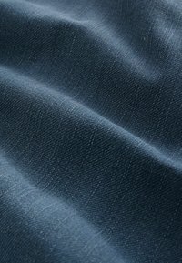 Tela de mezclilla azul oscuro con una textura suave, que presenta patrones de tejido diagonal y leves arrugas para dar profundidad y dimensión.