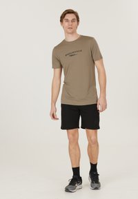 Bruine t-shirt met korte mouwen met "ENDURANCE" in het zwart gedrukt, gecombineerd met zwarte shorts en grijze sport schoenen, staand op een lichte achtergrond.