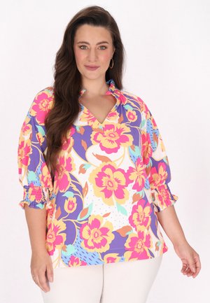 Multifarvet blomstret bluse med V-hals og korte puffede ærmer. Stoffet har pink, gul og lilla blomster på en hvid baggrund.