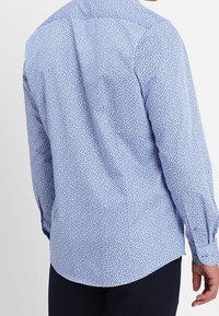 Jasnoniebieska koszula z małym kwiatowym nadrukiem, długimi rękawami i mankietami na guziki. Miękka tkanina, zaokrąglony dół i klasyczny kołnierzyk.