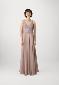 Duga, lepršava haljina od mekog mauve materijala s V-izrezom i ukrašenim korzetom. Ima tanke naramenice i elegantnu suknju.