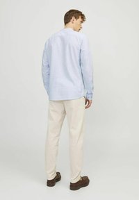 Camicia azzurro chiaro a maniche lunghe con polsi abbottonati, vestibilità slim e motivo a quadretti discreto, abbinata a pantaloni beige e scarpe marroni.