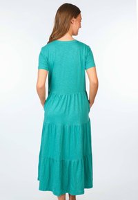 Tiefgrünes, gestuftes Maxikleid mit kurzen Ärmeln, das über einen runden Ausschnitt, eine weiche Textur und drei verschiedene Stoffschichten für ein fließendes Erscheinungsbild verfügt.