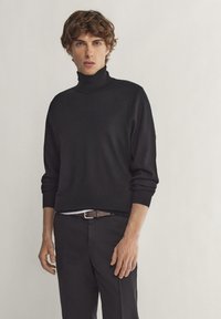 Schwarzer Rollkragenpullover aus weichem Strick, mit lockerer Passform und gerippten Bündchen. Kombiniert mit dunklen Hosen und einem braunen Gürtel. Schlichtes Design.