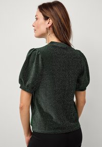 Donkergroene, glinsterende top met korte mouwen, puffmouwen en een ronde halslijn. Gladde textuur met een subtiel glanseffect.