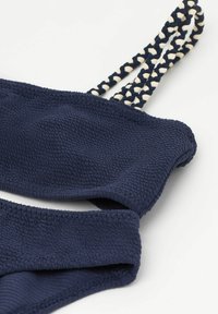 Marinblå badtopp med struktur och vävda krämfärgade remmar, som har en mjuk, formad design. Tyget har en lätt stretch för komfort.