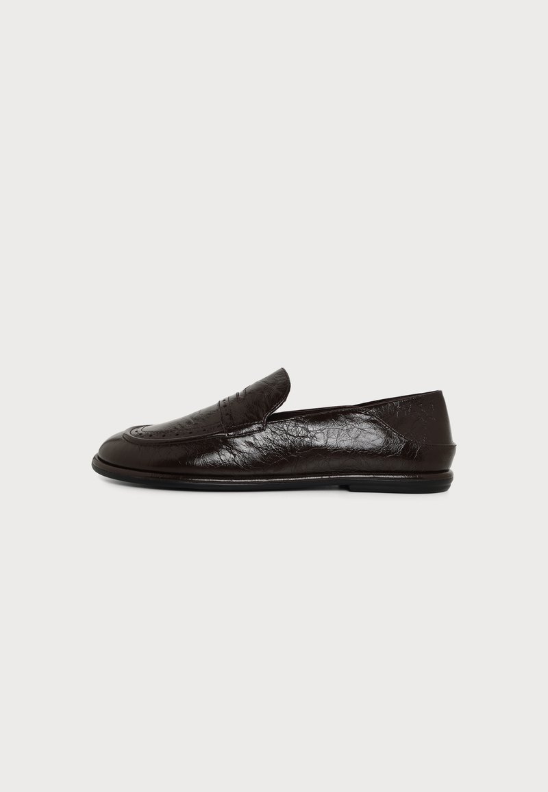 Chaussure mocassin noire en cuir brillant, à enfiler, avec un talon bas et un bout arrondi et lisse, vue de profil sur fond blanc.