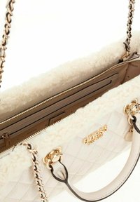 Bolso acolchado blanco con un forro interior de felpa beige, hardware dorado y correas de cadena. Presenta un compartimento con cremallera y detalles de marca.
