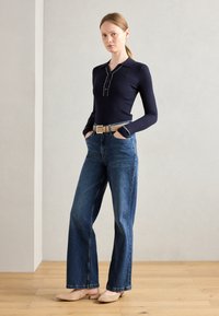 Navy ribbed long-sleeve top with front buttons, paired with high-waisted, wide-leg blue jeans and beige low-heeled shoes.
