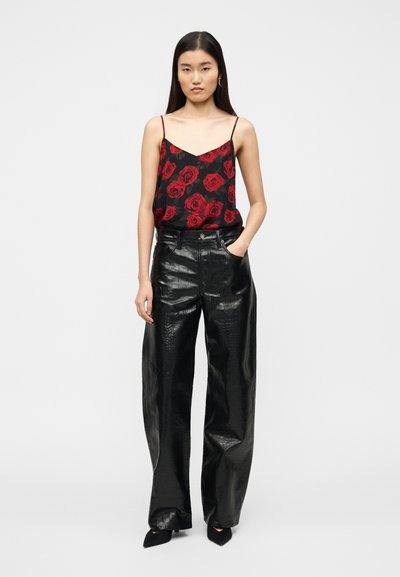 Μαύρο τοπ καμια με σχέδιο κόκκινο τριαντάφυλλο, συνδυασμένο με μαύρο, γυαλιστερό, ψεύτικο δερμάτινο παντελόνι με φαρδιά πόδια και ψηλή μέση. Μαύρες μυτερές ψηλοτάκουνες γόβες.