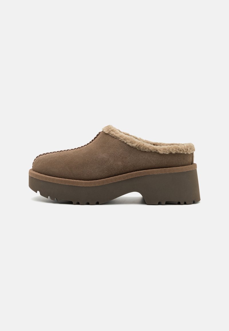 Sabot marron à enfiler avec une semelle épaisse et une doublure en fourrure beige autour de l’ouverture, montré de côté sur un fond uni.
