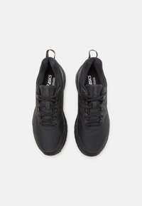 Zapatillas deportivas negras hechas de malla y materiales sintéticos. Cuentan con una parte superior texturizada, un sistema de cordones y tiradores en el talón para facilitar el calzado.