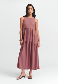 Maksi obleka v barvi prašnega rožnatega, ki ima brezrokavni kroj, nabrano pasovno linijo in tekoč silhueto. Lahkoten material z gladko teksturo.