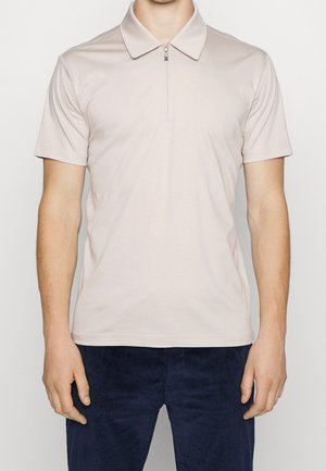 Polo met korte mouwen in lichtbeige met een ritssluiting bij de kraag. Soepele stoftextuur met subtiele stikdetails. Gecombineerd met marineblauwe ribfluwelen broek.