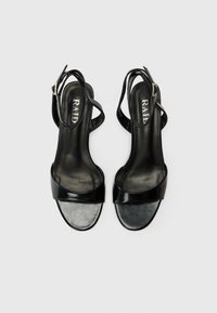 Sandales noires à talons avec une finition brillante, dotées d'une large bride à l'avant et d'une bride de cheville réglable. Texture lisse avec un éclat subtil.
