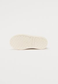 Semelle de chaussure en caoutchouc blanc avec un motif ondulé et une surface texturée ; comprend un détail de marque près du talon.