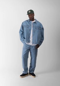 Šviesiai mėlynas džinsinis švarkas ir kelnės, derinami su balta marškinėliais ir tamsiais batais. Švarkas turi dideles kišenes ir laisvą siluetą.