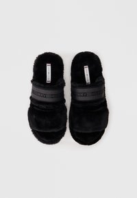 Schwarze Pelzschlappen mit einem breiten Texturriemen, der den Markennamen zeigt. Weiche Textur, offenes Zehendesign und gepolsterte Fußsohle.