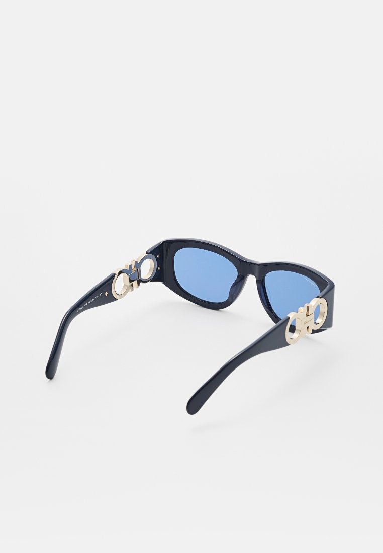 Marine Sonnenbrille mit blauen Gläsern, ausgestattet mit goldenen, runden Hardware-Akzenten an den Schläfen und einem eleganten, rechteckigen Rahmendesign.