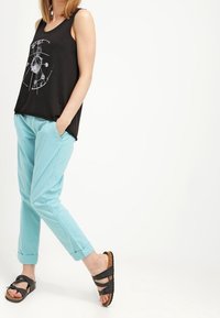 Svart ärmlös topp med grafiskt tryck, matchad med ljusblå byxor, uppvikta vid muddarna, och svarta sandaler med korsade remmar.