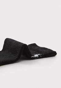 Calcetín de algodón negro con textura acanalada, doblado para exhibir el detalle del logo blanco. El material parece suave y duradero, diseñado para la comodidad.