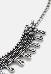 Sølv metal halskæde med indviklet fletdesign, runde perler og dekorative påfuglefjer accenter. Har en klassisk kædelukning.