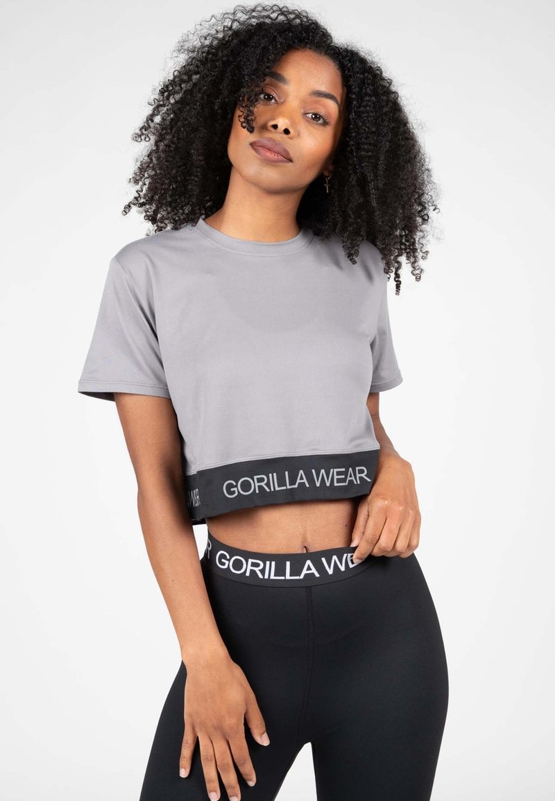 Grijze cropped t-shirt van gladde stof met een zwarte band met het "GORILLA WEAR" logo, gecombineerd met zwarte leggings.