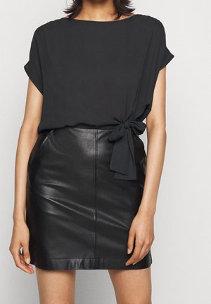 Sort top med korte ærmer og et knudedetalje ved taljen, kombineret med en tætsiddende sort lædernederdel. Glat tekstur med et elegant design.