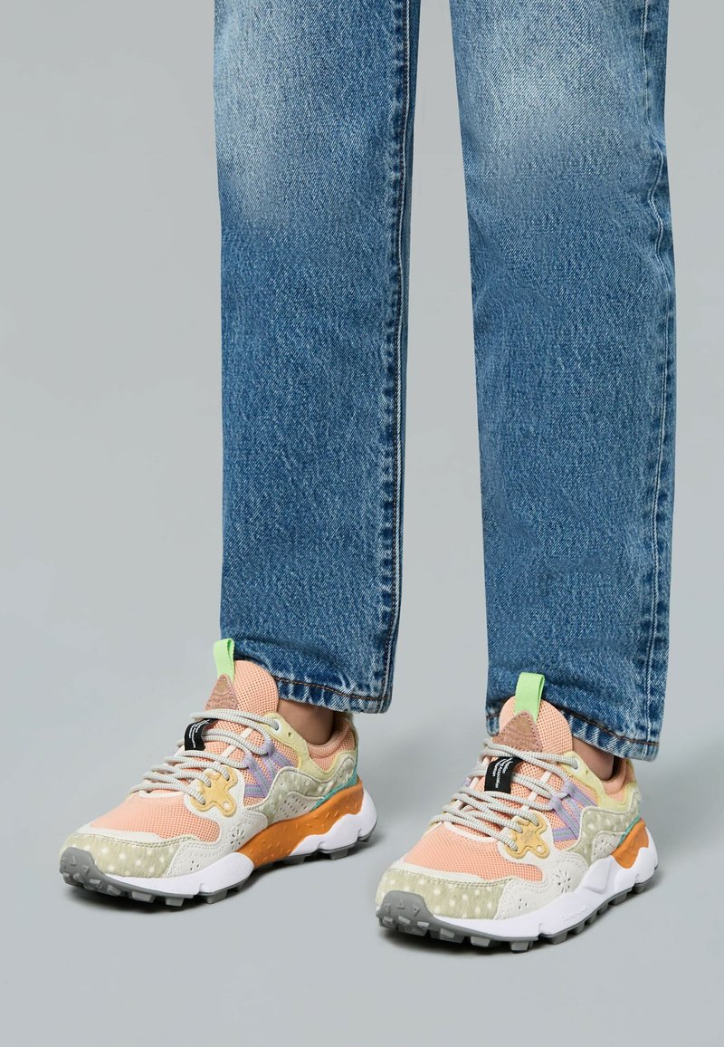 Mehrfarbige Sneaker mit einer Mischung aus pinkem Mesh, beigen Akzenten und einer orangefarbenen Sohle, die mit strukturierten Mustern und kontrastierenden Schnürsenkeln versehen ist.