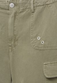 Khaki cargobroek met een gladde textuur, voorzien van een voorzak, knoopsluiting en twee decoratieve zilveren ogen.