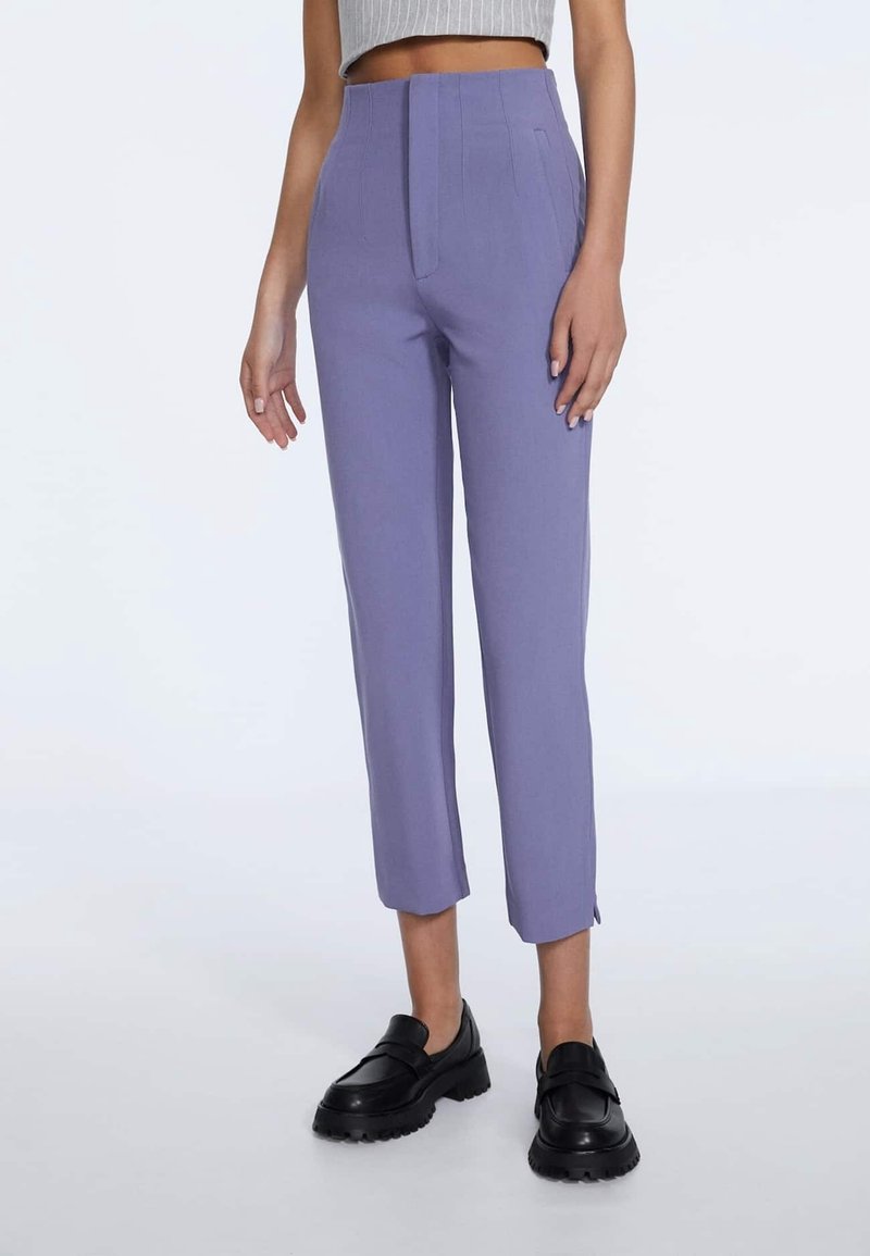 Pantalons sur mesure, taille haute, en tissu lavande doux, présentant des plis à l'avant, une longueur raccourcie et des fentes latérales, assortis à des chaussures noires.