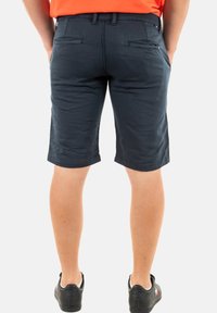 Donkerblauwe katoenen shorts met een rechte snit, twee achterzakken en een platte tailleband, die net boven de knie eindigen. Draag ze met zwarte schoenen.