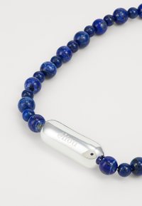 Μπλε βραχιόλι από λάπις λάζουλι με γυαλιστερή ασημένια λεπτομέρεια που φέρει εγχαραγμένο κείμενο, παρουσιάζοντας στρογγυλές χάντρες διαφόρων μεγεθών και λεία υφή.