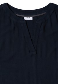 Blouse bleu marine foncé avec un col rond, une fente en V centrale et une étiquette blanche portant la mention « CECIL » à l'intérieur du col.