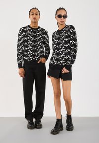 Sorte strikkegenser med hvitt blomster mønster, kombinert med sorte bukser og shorts. Begge har på seg sorte militærstøvler og solbriller.