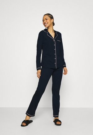 Donkerblauw pyjama set met roze bies. Bevat een button-up shirt en rechte pijpen. Glad materiaal met lange mouwen en een zakdetails.