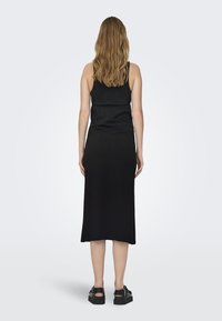Robe maxi sans manches noire avec un buste ajusté et une jupe fluide, fabriquée en tissu doux. Des sandales à semelle épaisse complètent l'ensemble.