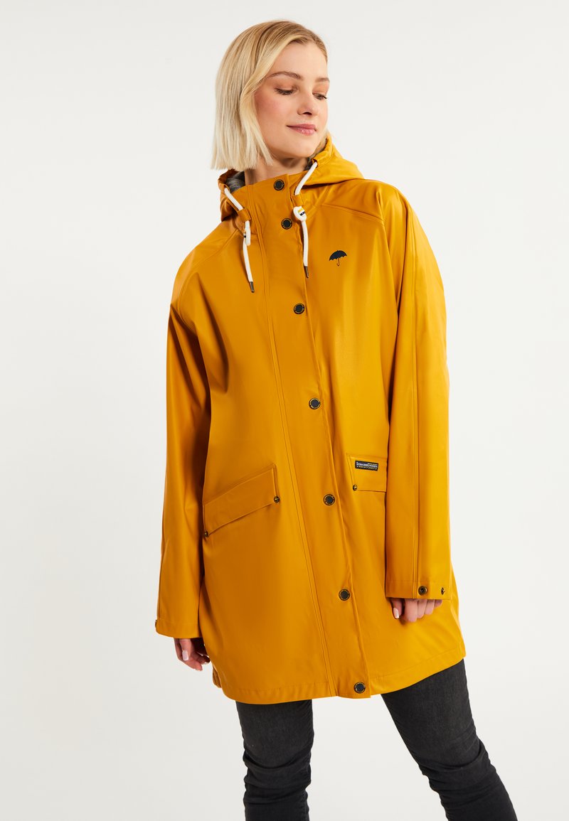 Chaqueta de lluvia amarilla impermeable con capucha, que cuenta con botones a presión, dos bolsillos frontales y un logo en el pecho. Textura suave y hasta la rodilla.