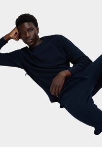 Maglione a coste blu navy e pantaloni abbinati, caratterizzati da una vestibilità comoda con maniche lunghe. Tessuto dalla texture liscia, design minimalista.