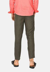 Pantaloni in lino verde oliva a taglio dritto, caratterizzati da una trama liscia e una vestibilità comoda. Indossati con sandali neri e una maglietta corallo.