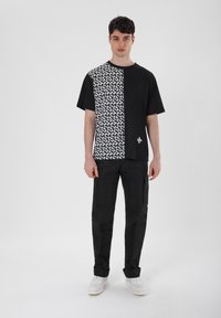 Schwarz-weiße T-Shirt mit einem geometrischen Muster auf einer Hälfte, einfarbig schwarz auf der anderen, Rundhalsausschnitt und kurzen Ärmeln.