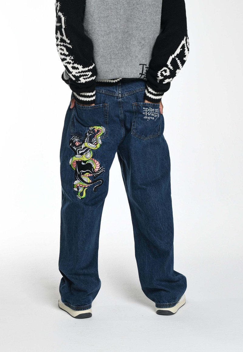 Jeans in denim blu ampi con ricamo colorato di una pantera e di un serpente sulla coscia sinistra, dotati di tasche posteriori e dettaglio del logo.