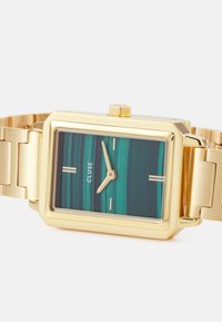 Gold rectangular watch with a teal striped dial, featuring minimalist hour markers and gold hands, secured by a gold link bracelet.