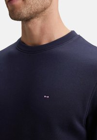 Sweatshirt col rond marine en mélange de coton, avec un petit logo rose sur la poitrine. Texture lisse avec un col et des poignets côtelés.