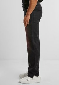 Pantalones de mezclilla negra con un corte recto, que cuentan con cinco bolsillos y una textura suave, combinados con zapatillas blancas con detalles del logo.