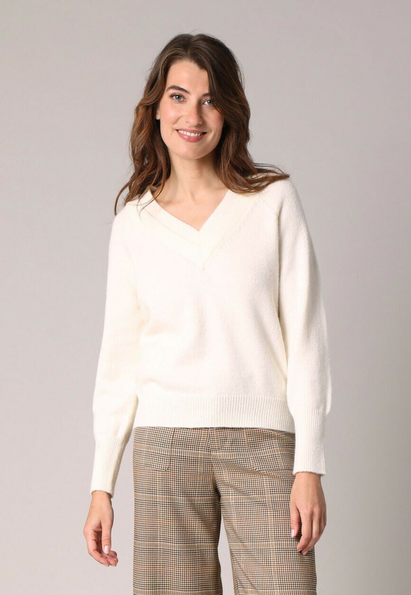Pull blanc à col en V en tissu doux et texturé avec des manches longues et un ourlet côtelé ; associé à un pantalon carré marron.