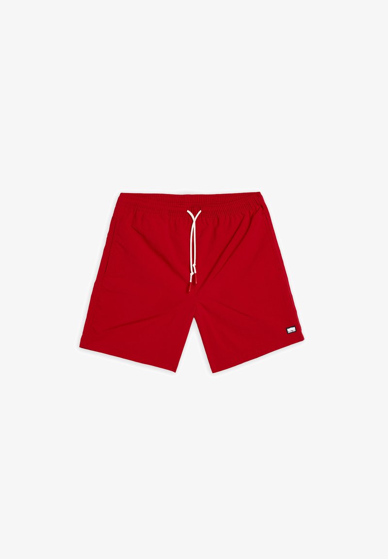 Punaiset uimaportsarit, jotka on valmistettu nopeasti kuivuvasta kankaasta. Niissä on joustava vyötärö, jonka sisällä on nyöri, sekä sivutaskut. Neliön muotoinen logo-etiketti alhaalla vasemmalla.