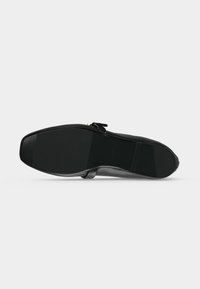 Chaussure en cuir noir avec un bout carré et une semelle lisse, vue par le dessous sur un fond blanc.